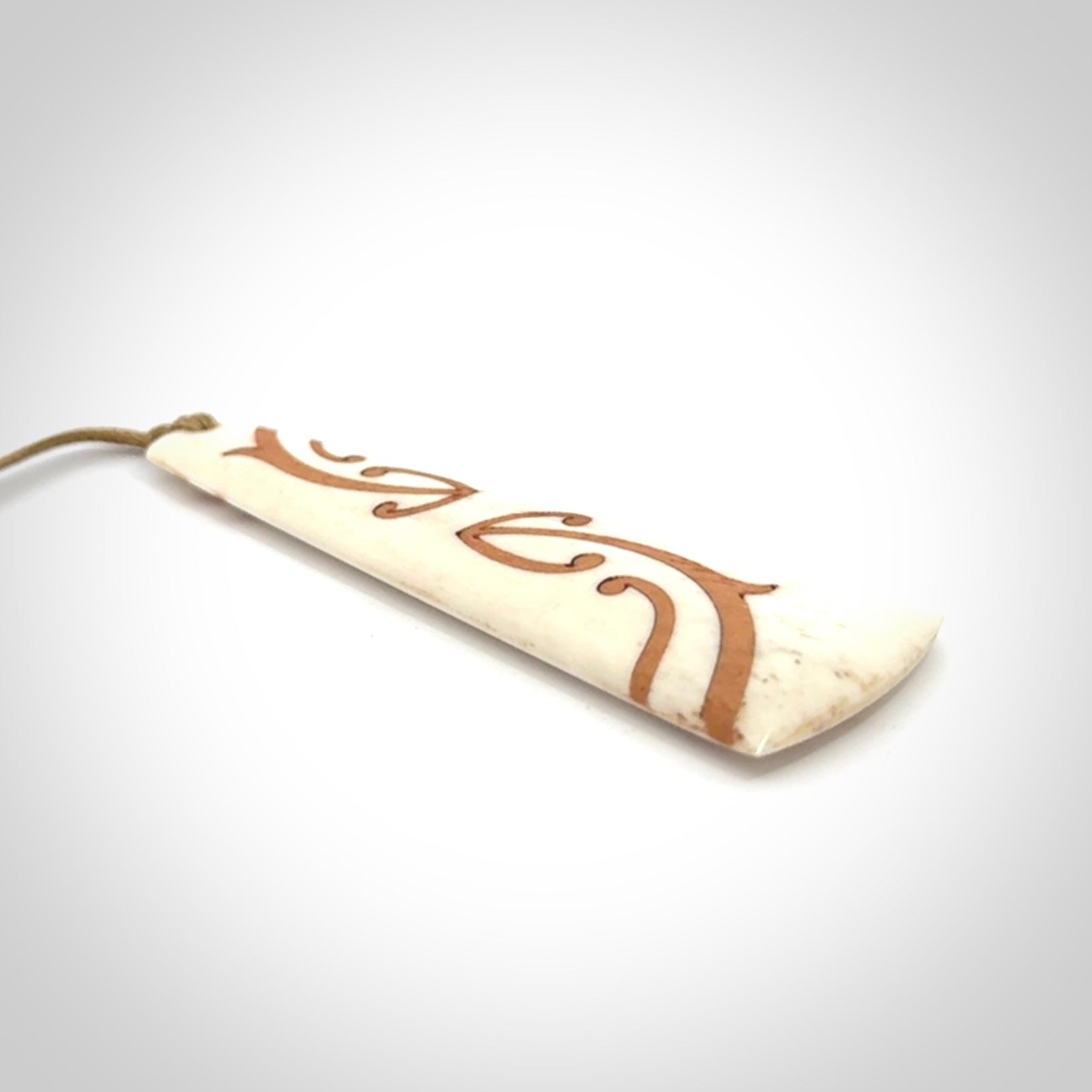 A hand carved, double sided, bone toki with triple koru, intricate pendant. The cord is a camel colour and is adjustable.