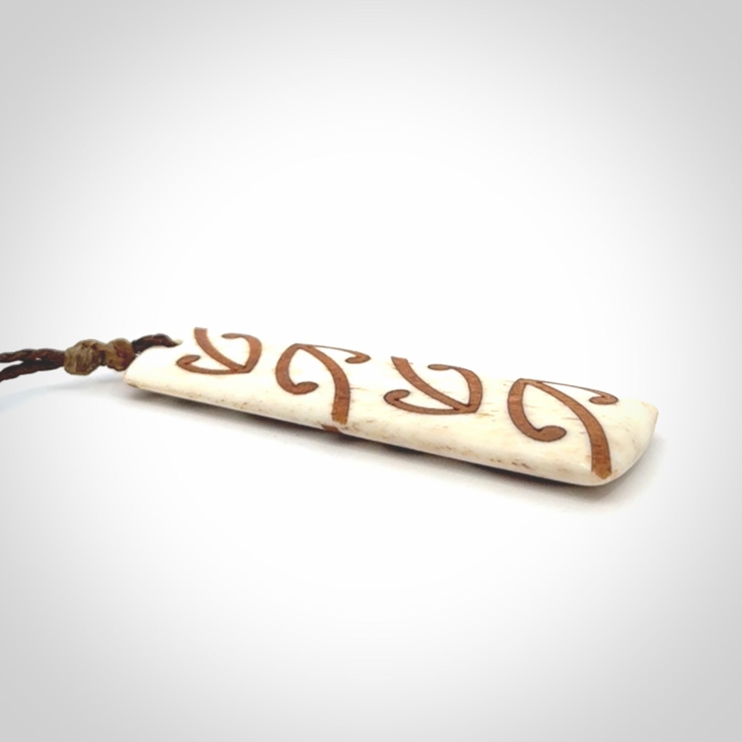 A hand carved, double sided, bone toki with triple koru, intricate pendant. The cord is a brown colour and is adjustable.