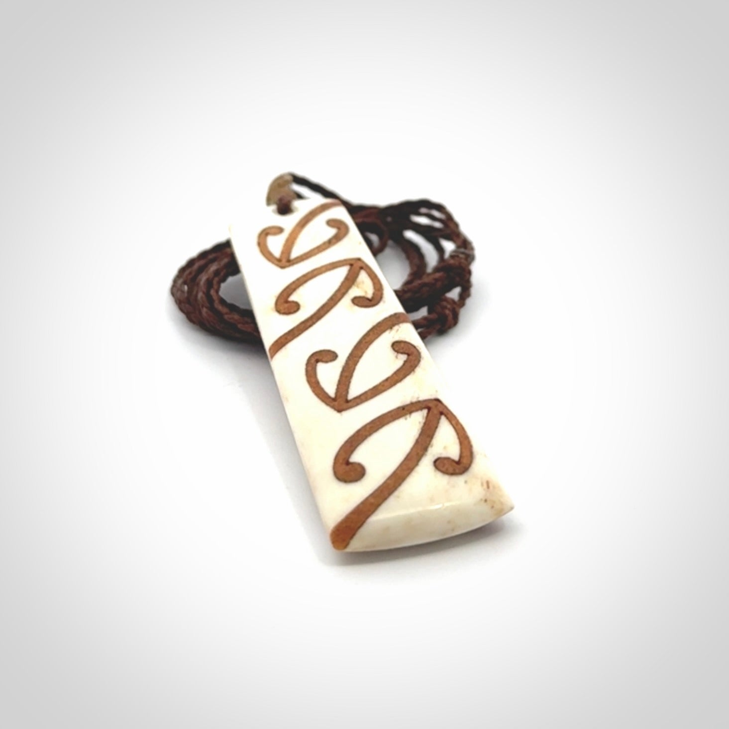 A hand carved, double sided, bone toki with triple koru, intricate pendant. The cord is a brown colour and is adjustable.