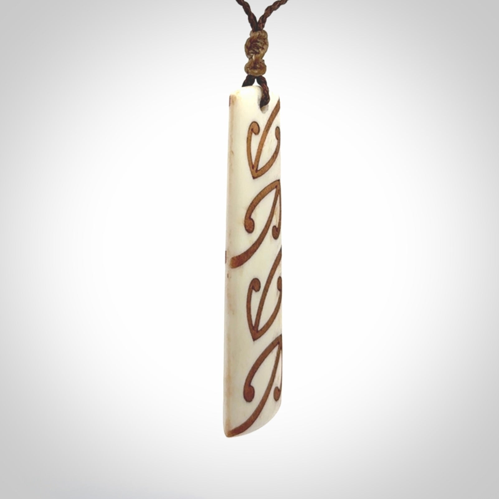 A hand carved, double sided, bone toki with triple koru, intricate pendant. The cord is a brown colour and is adjustable.