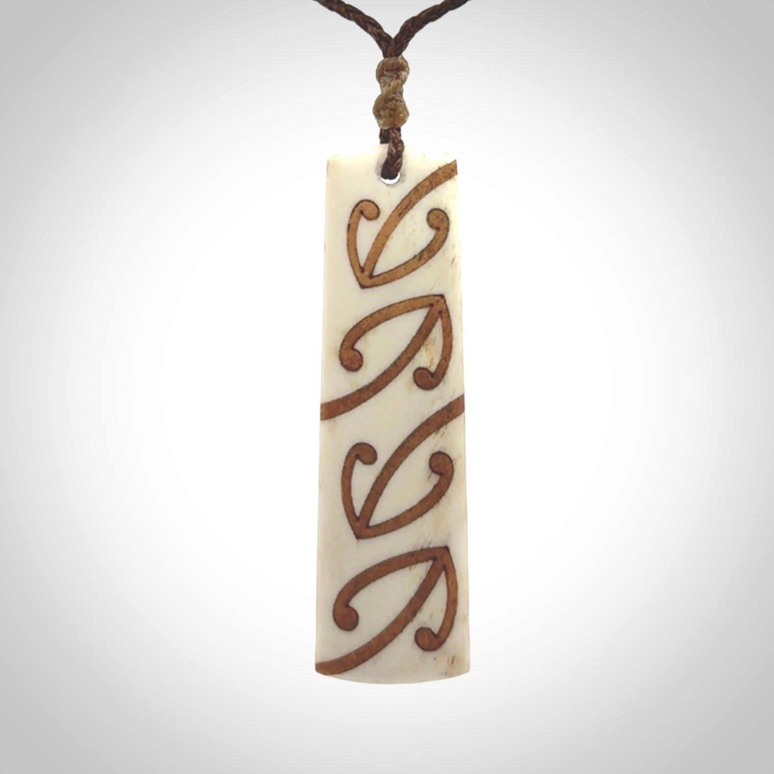 A hand carved, double sided, bone toki with triple koru, intricate pendant. The cord is a brown colour and is adjustable.