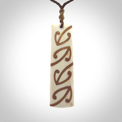 A hand carved, double sided, bone toki with triple koru, intricate pendant. The cord is a brown colour and is adjustable.