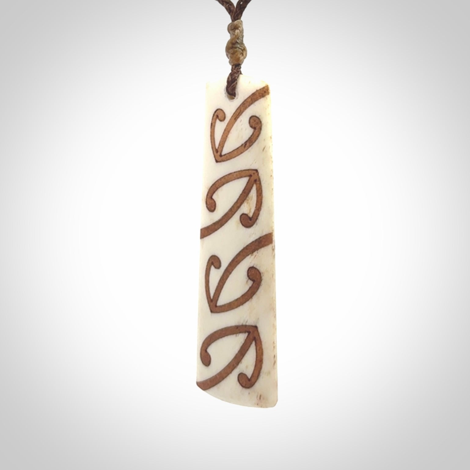 A hand carved, double sided, bone toki with triple koru, intricate pendant. The cord is a brown colour and is adjustable.
