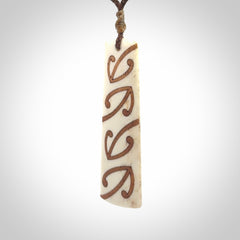 A hand carved, double sided, bone toki with triple koru, intricate pendant. The cord is a brown colour and is adjustable.