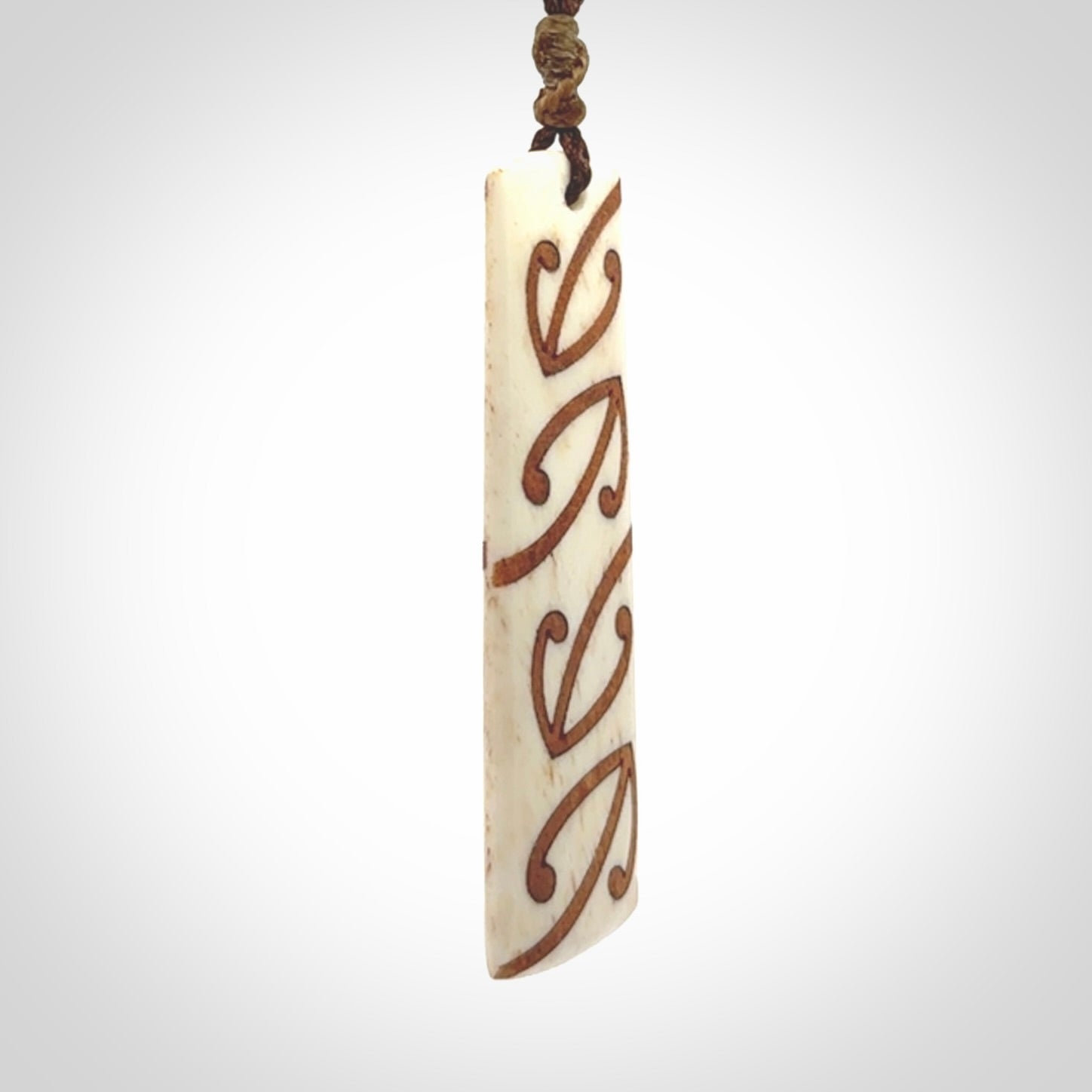A hand carved, double sided, bone toki with triple koru, intricate pendant. The cord is a brown colour and is adjustable.