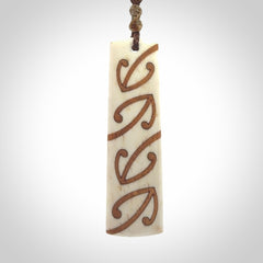 A hand carved, double sided, bone toki with triple koru, intricate pendant. The cord is a brown colour and is adjustable.