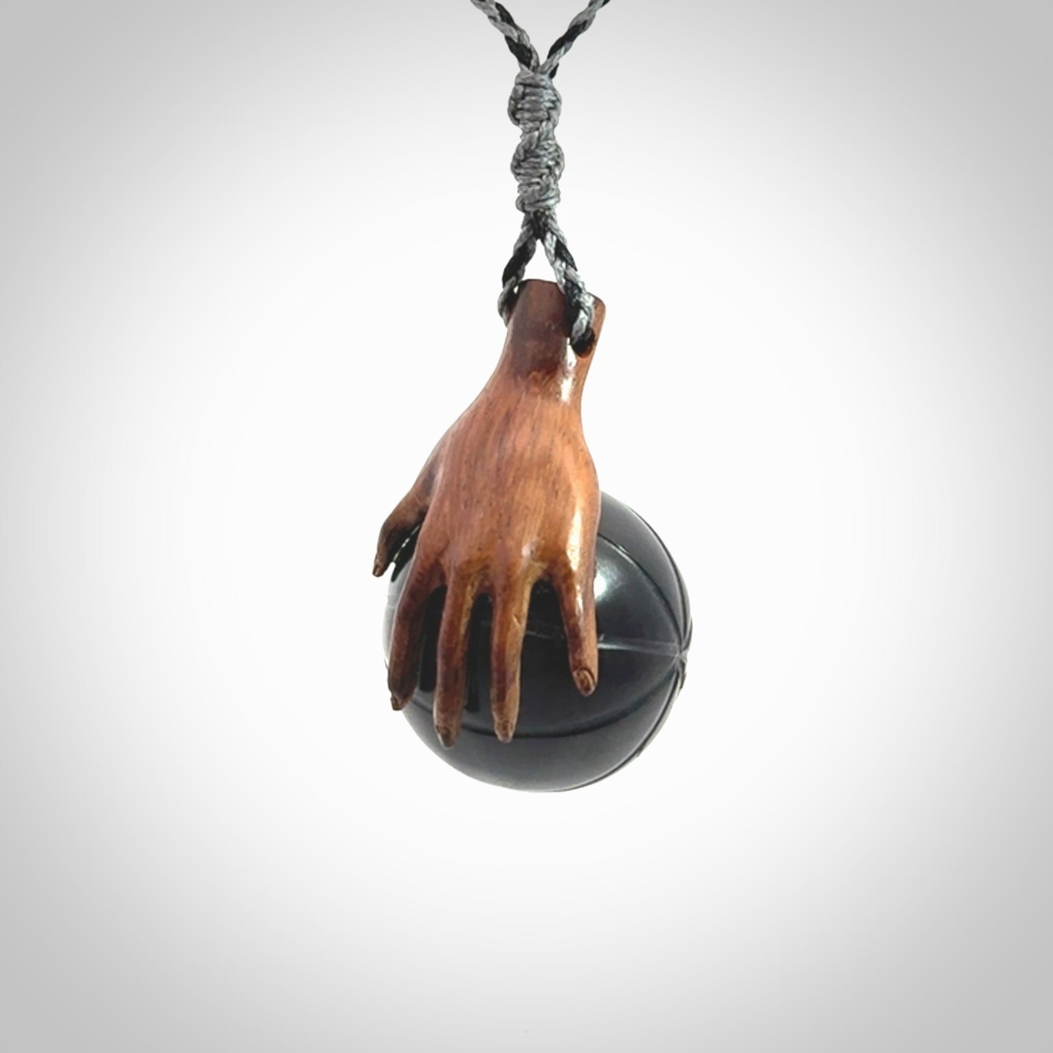 This is a very cool pendant that we've had carved for all you Basketball fans. This is a pendant with a wooden hand holding a black jade basketball. We provide this on an adjustable cord, and we ship worldwide