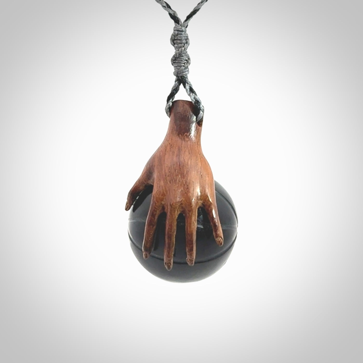 This is a very cool pendant that we've had carved for all you Basketball fans. This is a pendant with a wooden hand holding a black jade basketball. We provide this on an adjustable cord, and we ship worldwide
