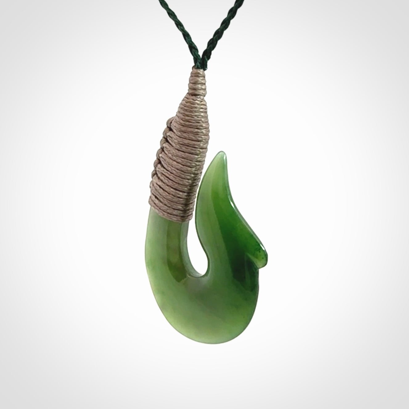 This photo shows a greenstone hook, or matau, pendant. It is a beautiful green British Columbia jade stone. The plaited cord is a green colour. It is plaited and the length can be adjusted.