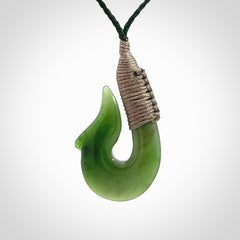 This photo shows a greenstone hook, or matau, pendant. It is a beautiful green British Columbia jade stone. The plaited cord is a green colour. It is plaited and the length can be adjusted.