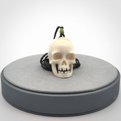 This picture shows a large sized Deer Antler Bone skull pendant that we have hand carved. It is polished to a soft shine and is a very striking piece. The cord is black and has a small green popper binding just above the pendant.