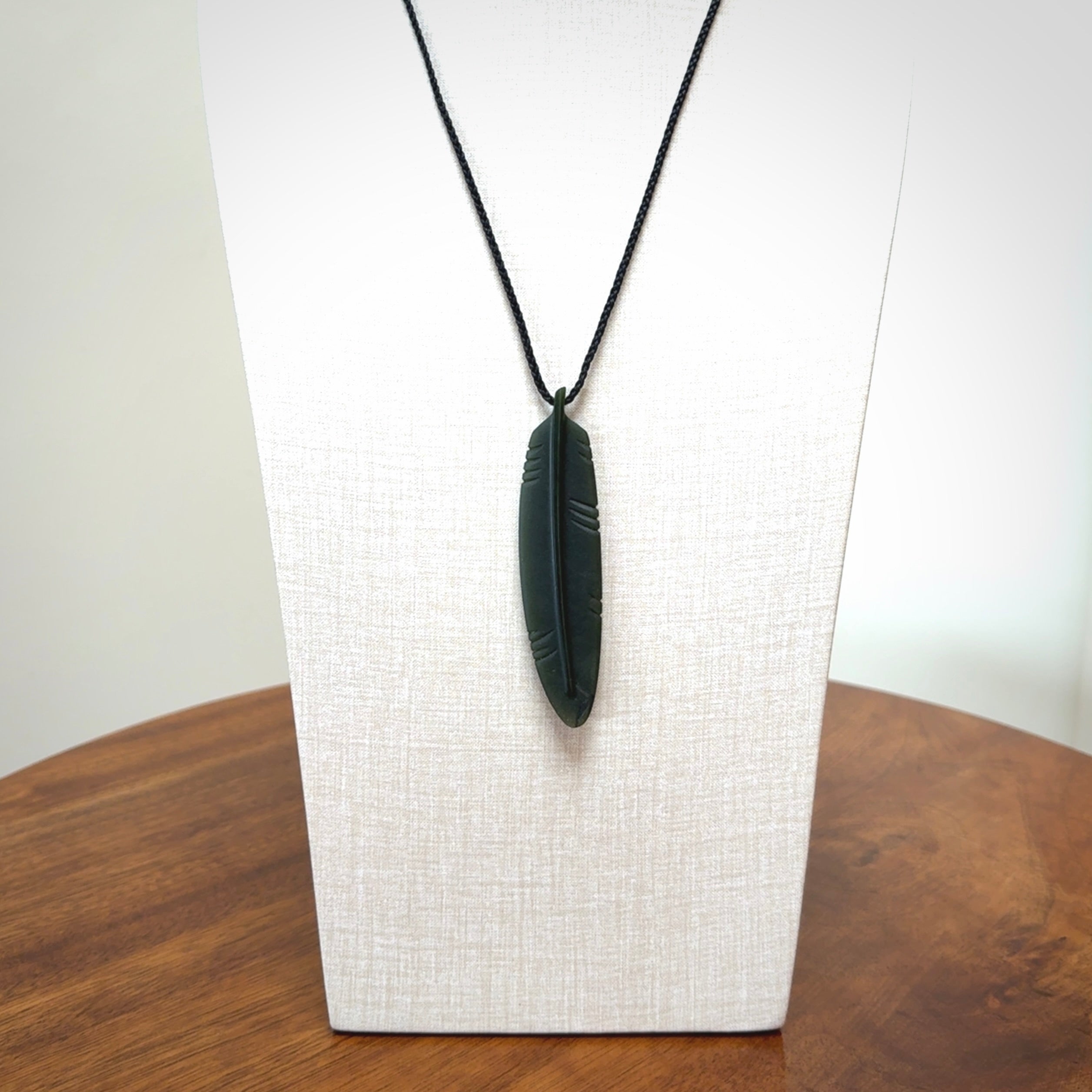 A hand carved large New Zealand Jade feather necklace. The cord is a black colour and is a fixed length. A large sized hand made Jade feather necklace by New Zealand artist Kerry Thompson. One off work of art to wear.