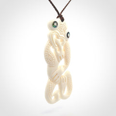 Hand carved bone Tiki pendant. Traditional art hand carved for NZ Pacific. Bone Tiki necklace with Paua Shell eyes. Delivered with Express Courier. Provided with adjustable cords and packaged in a woven kete pouch.