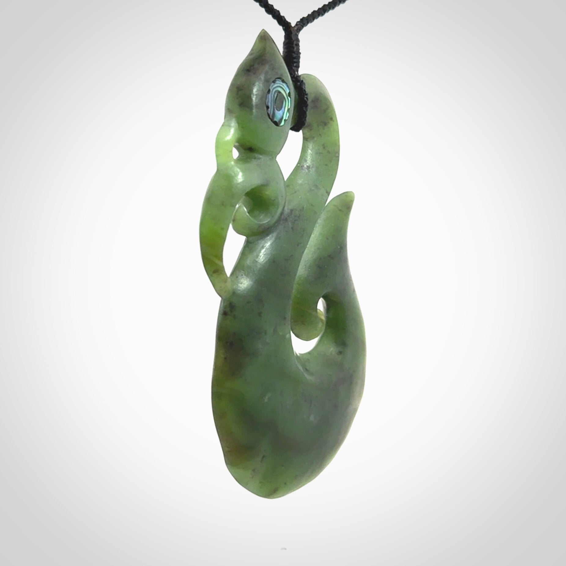 This picture shows a large traditional manaia pendant carved in New Zealand Jade with Paua shell eyes.