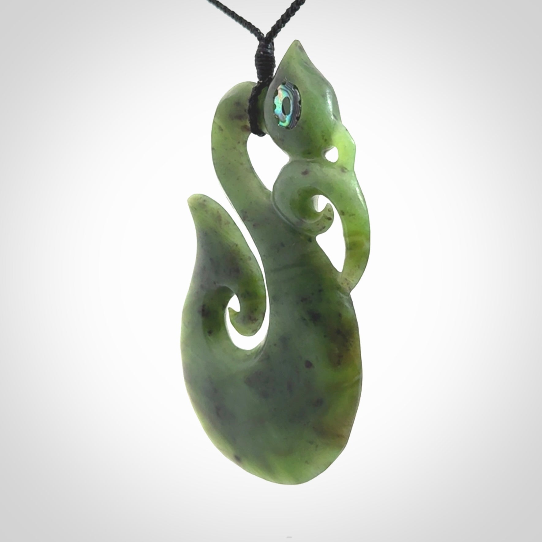 This picture shows a large traditional manaia pendant carved in New Zealand Jade with Paua shell eyes.