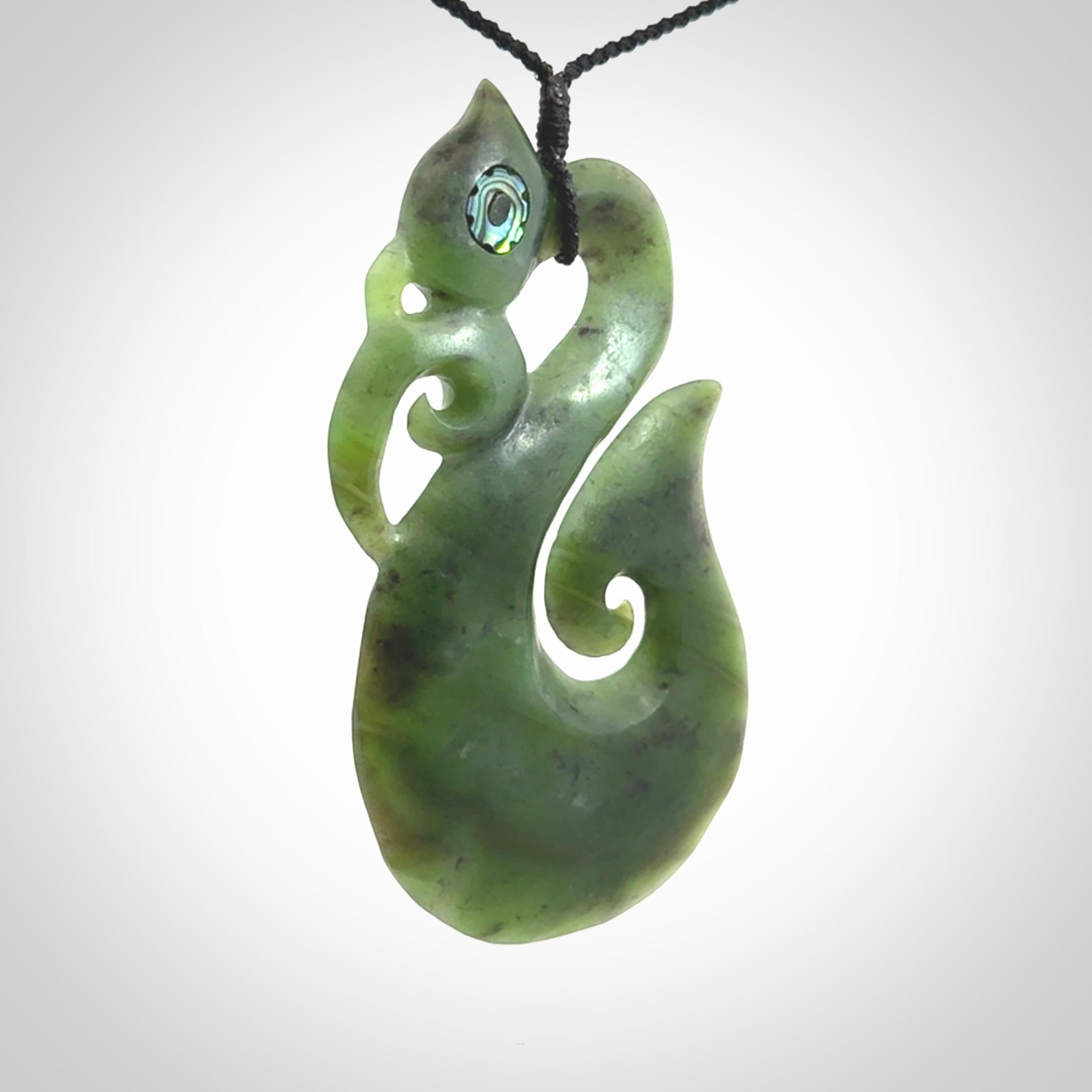 This picture shows a large traditional manaia pendant carved in New Zealand Jade with Paua shell eyes.