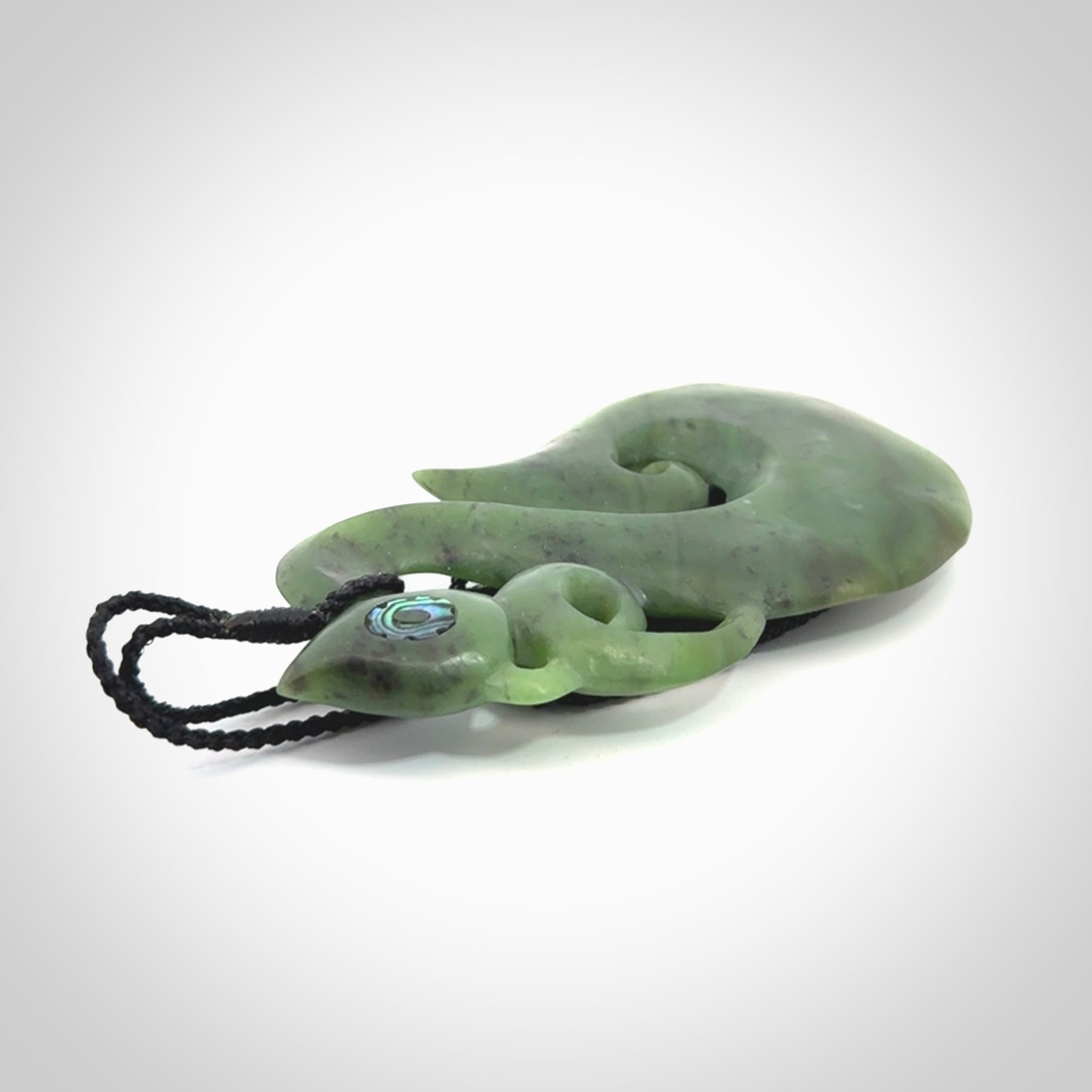 This picture shows a large traditional manaia pendant carved in New Zealand Jade with Paua shell eyes.