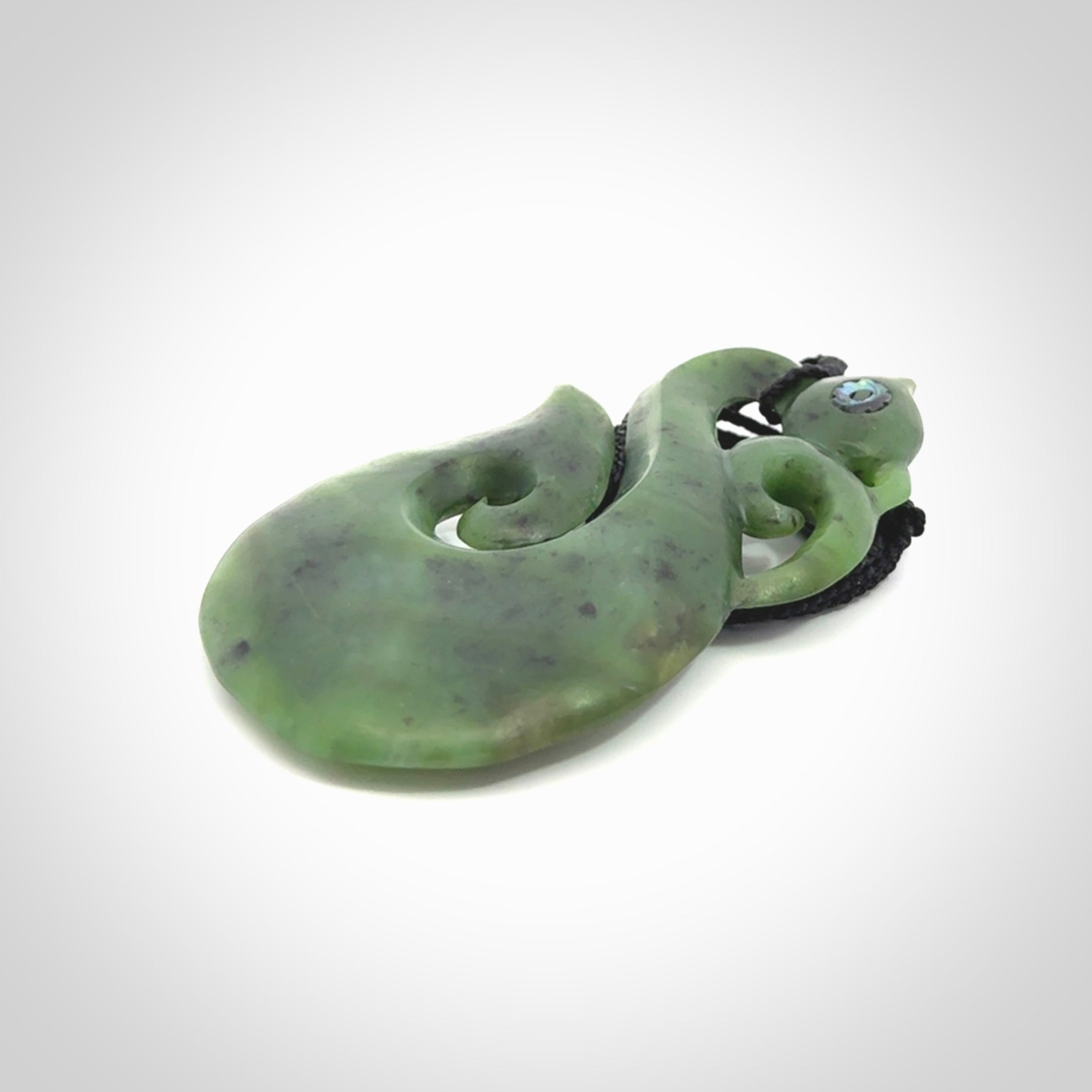 This picture shows a large traditional manaia pendant carved in New Zealand Jade with Paua shell eyes.