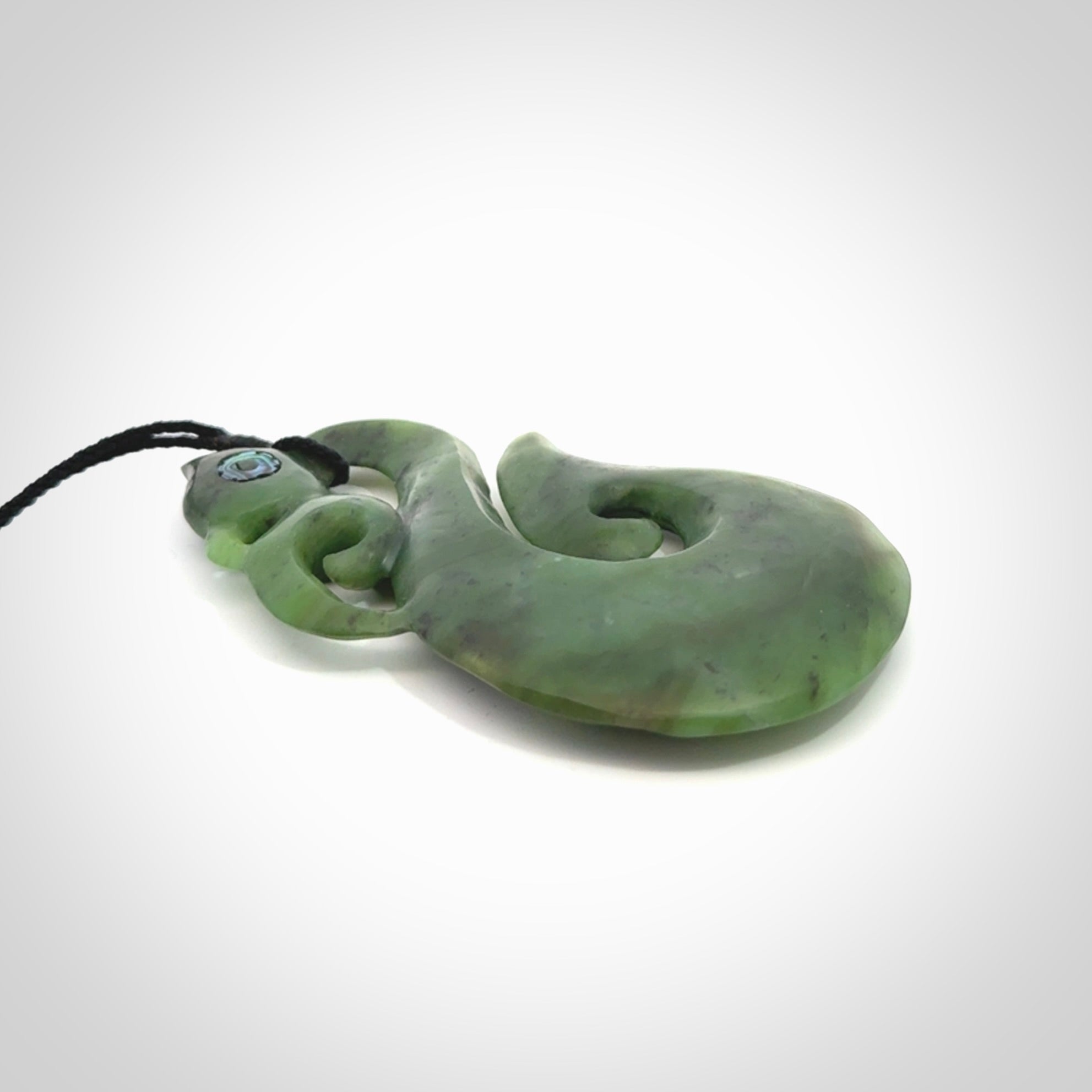 This picture shows a large traditional manaia pendant carved in New Zealand Jade with Paua shell eyes.