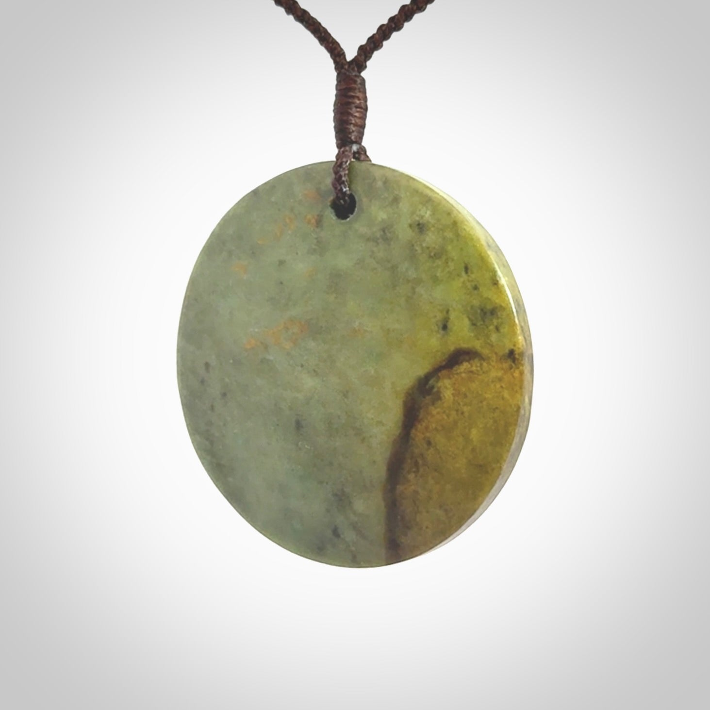 This piece is a large sized, oval round, disc pendant. It is suspended on a chocolate brown coloured braided cord that is length adjustable.