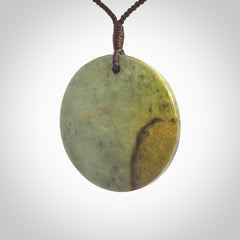 This piece is a large sized, oval round, disc pendant. It is suspended on a chocolate brown coloured braided cord that is length adjustable.