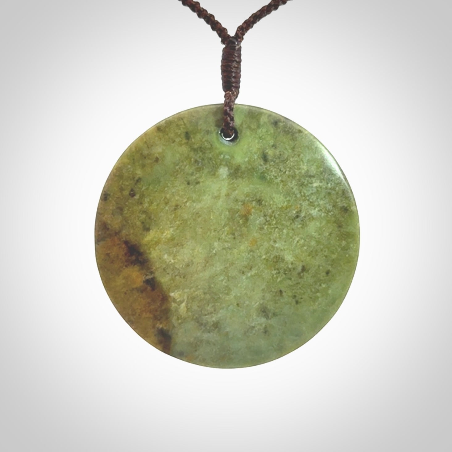 This piece is a large sized, oval round, disc pendant. It is suspended on a chocolate brown coloured braided cord that is length adjustable.