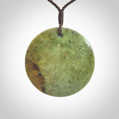 This piece is a large sized, oval round, disc pendant. It is suspended on a chocolate brown coloured braided cord that is length adjustable.