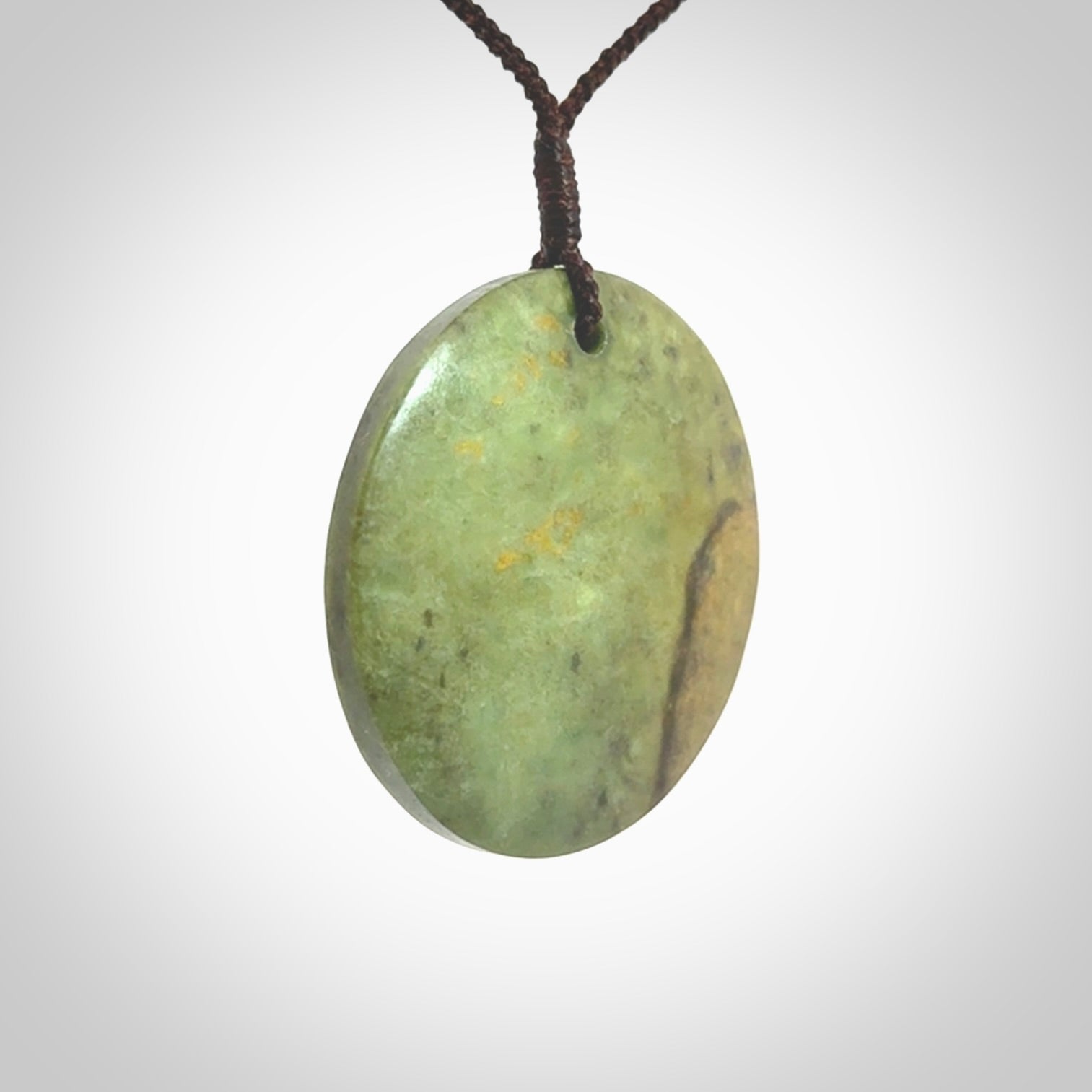 This piece is a large sized, oval round, disc pendant. It is suspended on a chocolate brown coloured braided cord that is length adjustable.