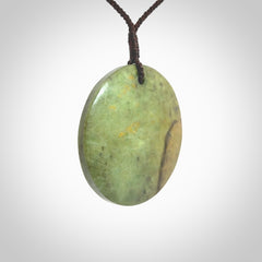 This piece is a large sized, oval round, disc pendant. It is suspended on a chocolate brown coloured braided cord that is length adjustable.