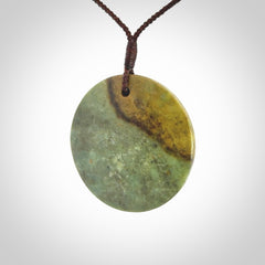 This piece is a large sized, oval round, disc pendant. It is suspended on a chocolate brown coloured braided cord that is length adjustable.