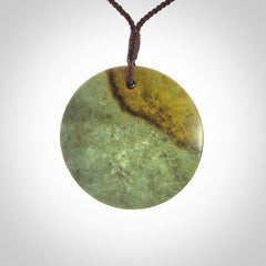 This piece is a large sized, oval round, disc pendant. It is suspended on a chocolate brown coloured braided cord that is length adjustable.