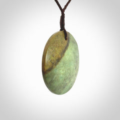 This piece is a large sized, oval round, disc pendant. It is suspended on a chocolate brown coloured braided cord that is length adjustable.