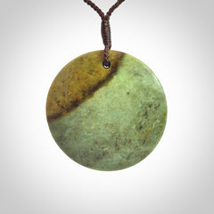 This piece is a large sized, oval round, disc pendant. It is suspended on a chocolate brown coloured braided cord that is length adjustable.