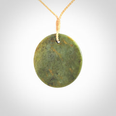 This piece is a medium sized, oval round, disc pendant. It is suspended on a beige coloured braided cord that is length adjustable.