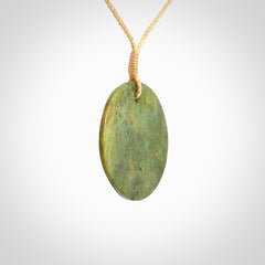 This piece is a medium sized, oval round, disc pendant. It is suspended on a beige coloured braided cord that is length adjustable.