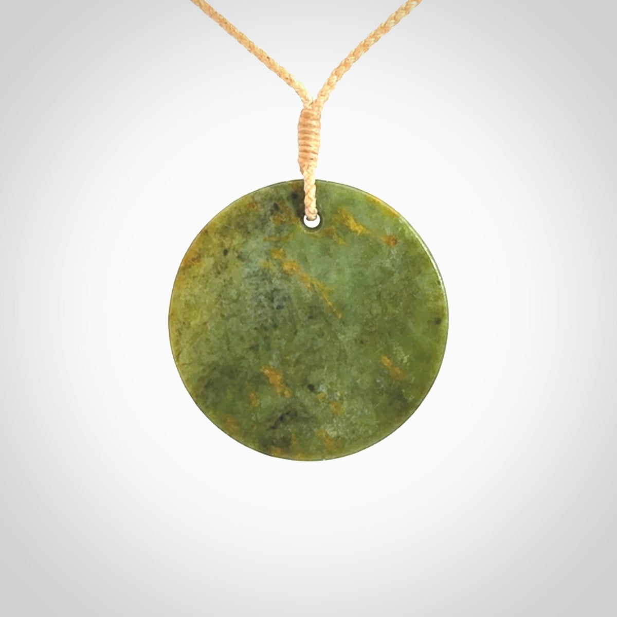 This piece is a medium sized, oval round, disc pendant. It is suspended on a beige coloured braided cord that is length adjustable.