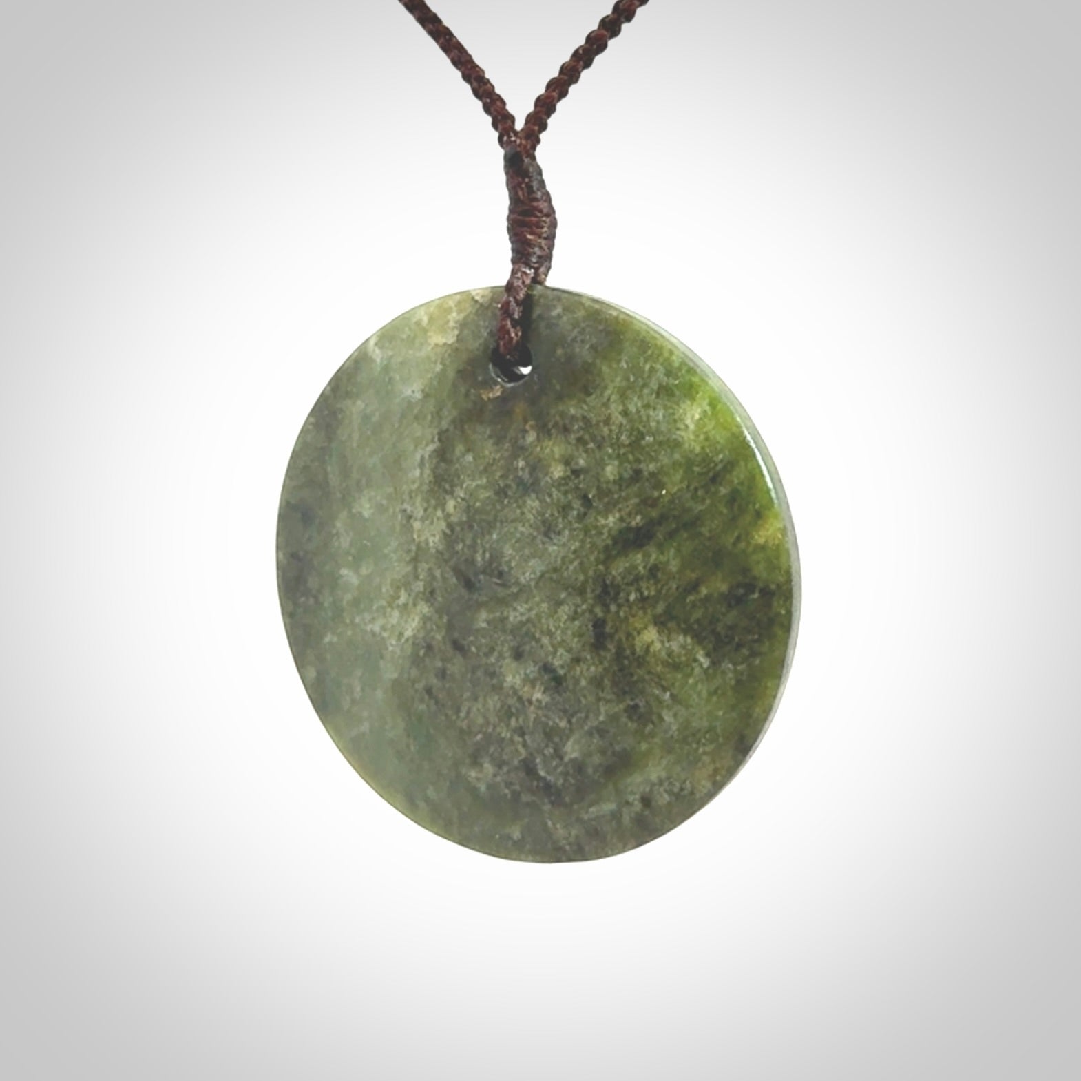 This piece is a large sized, oval round, disc pendant. It is suspended on a brown coloured braided cord that is length adjustable.