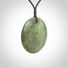 This piece is a large sized, oval round, disc pendant. It is suspended on a brown coloured braided cord that is length adjustable.
