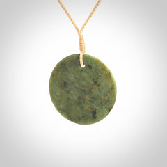 This piece is a medium sized, oval round, disc pendant. It is suspended on a beige coloured braided cord that is length adjustable.
