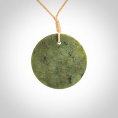 This piece is a medium sized, oval round, disc pendant. It is suspended on a beige coloured braided cord that is length adjustable.