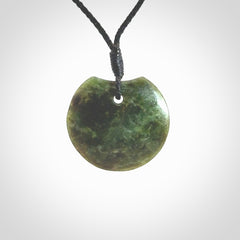 This piece is a small sized, oval round, disc pendant. It is suspended on a black coloured braided cord that is length adjustable.