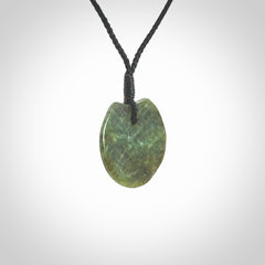 This piece is a small sized, oval round, disc pendant. It is suspended on a black coloured braided cord that is length adjustable.