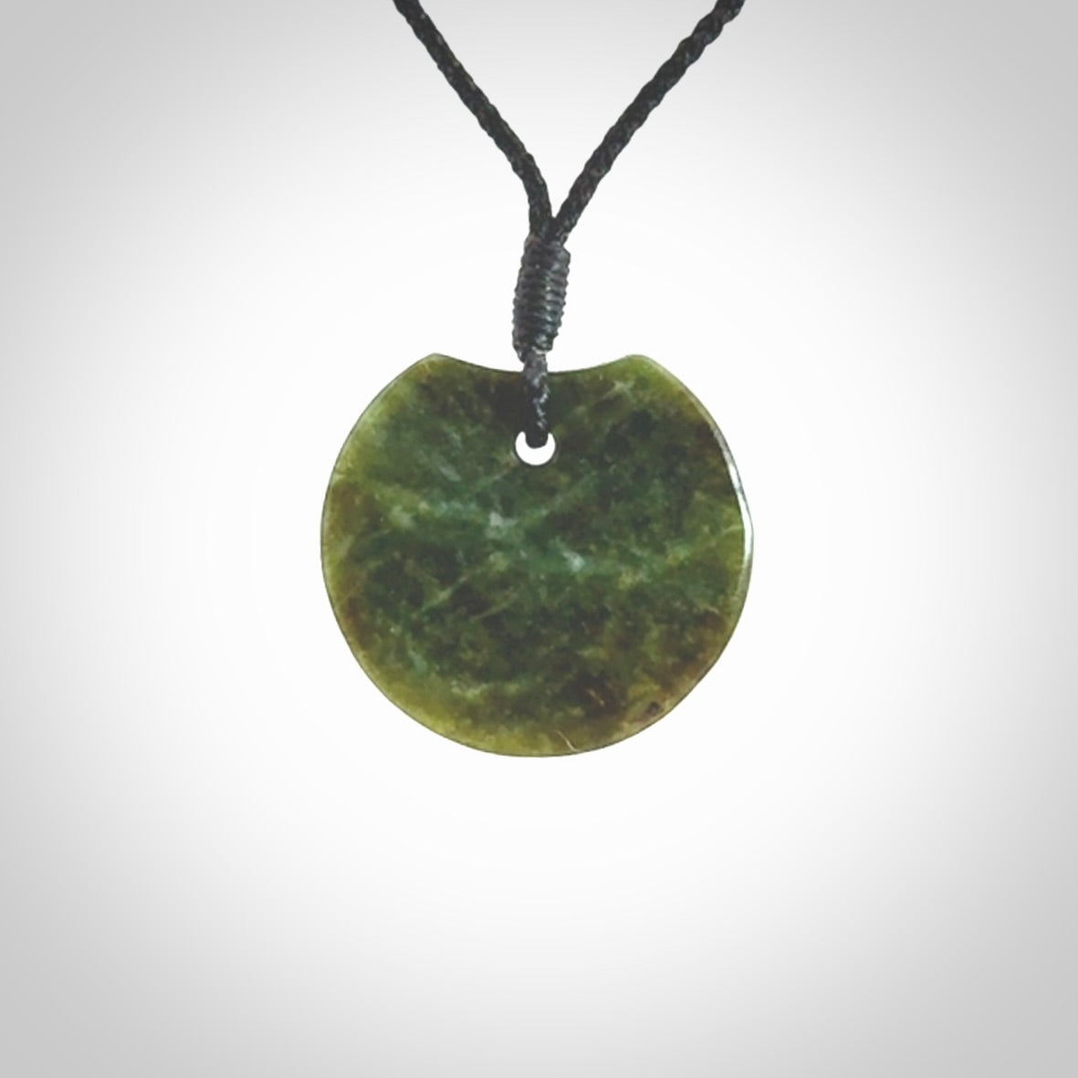 This piece is a small sized, oval round, disc pendant. It is suspended on a black coloured braided cord that is length adjustable.