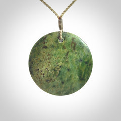 This piece is a large sized, oval round, disc pendant. It is suspended on a khaki coloured braided cord that is length adjustable.