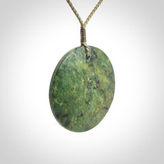 This piece is a large sized, oval round, disc pendant. It is suspended on a khaki coloured braided cord that is length adjustable.