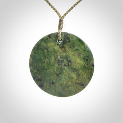 This piece is a large sized, oval round, disc pendant. It is suspended on a khaki coloured braided cord that is length adjustable.