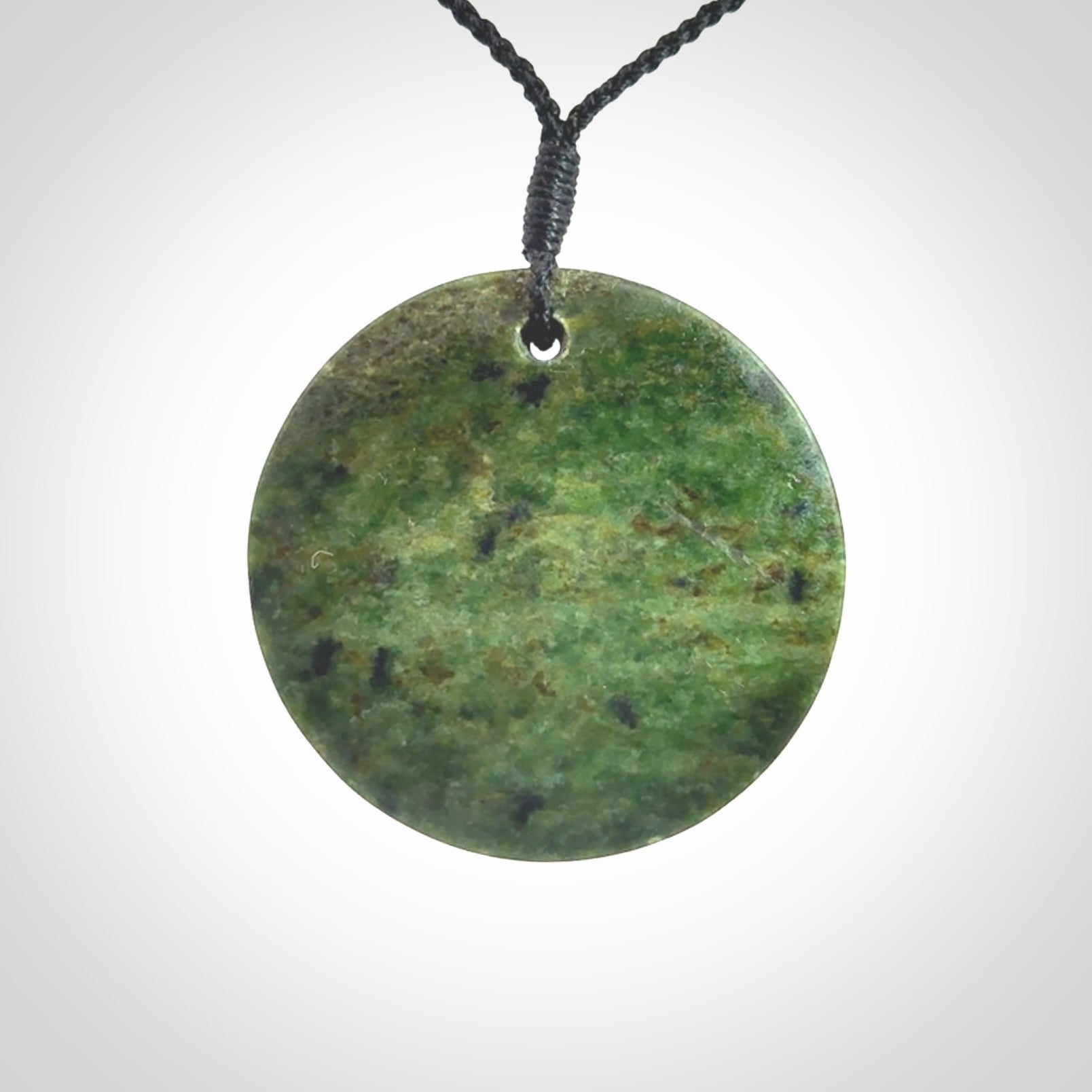 This piece is a large sized, oval round, disc pendant. It is suspended on a black coloured braided cord that is length adjustable.