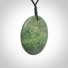 This piece is a large sized, oval round, disc pendant. It is suspended on a black coloured braided cord that is length adjustable.