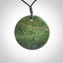 This piece is a large sized, oval round, disc pendant. It is suspended on a black coloured braided cord that is length adjustable.