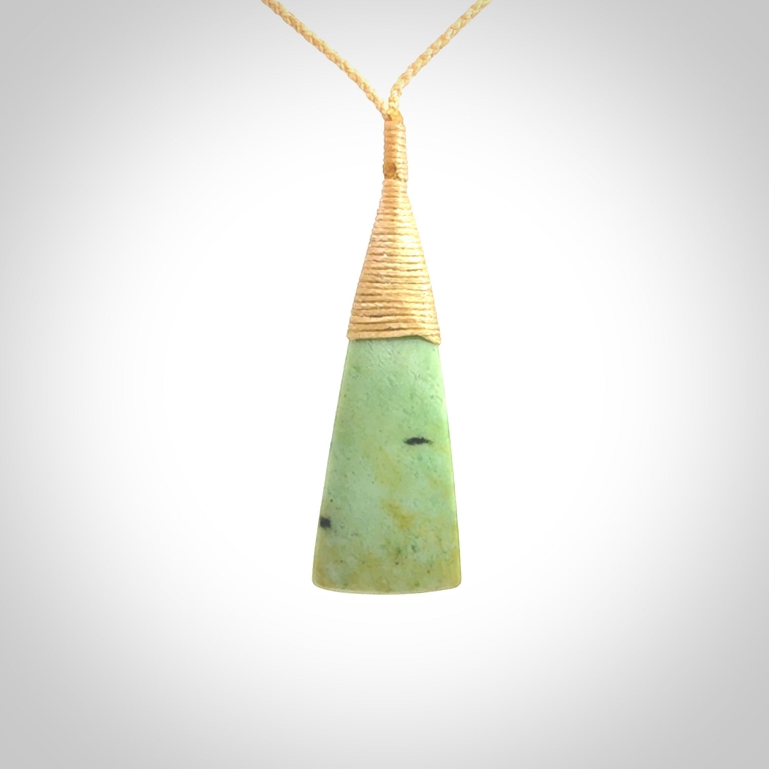 This photo shows a medium sized jade drop shaped pendant. It a a lovely varied green and light orange New Zealand Flower jade. The cord is a four plait beige and is adjustable in length.